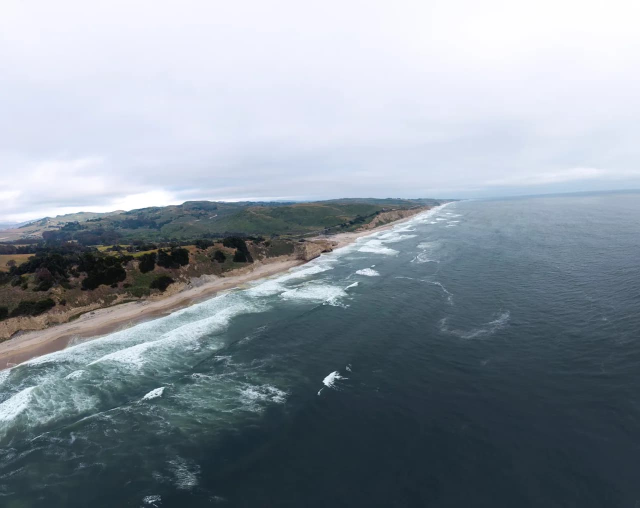Lines of surf follow a long beach between wooded hills and gray-blue water. Coast & City photo 4 of 11.