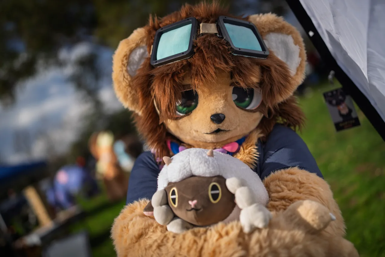 A person in a brown animal costume wears large square goggles and holds a small plush sheep. Costumes photo 10 of 20.