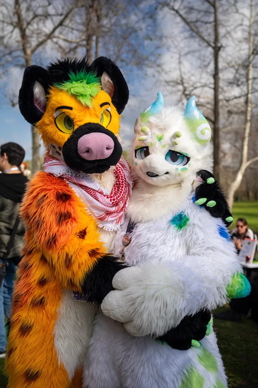 Two people in orange and black and white and green animal costumes pose together beneath bare trees. Costumes photo 11 of 20.